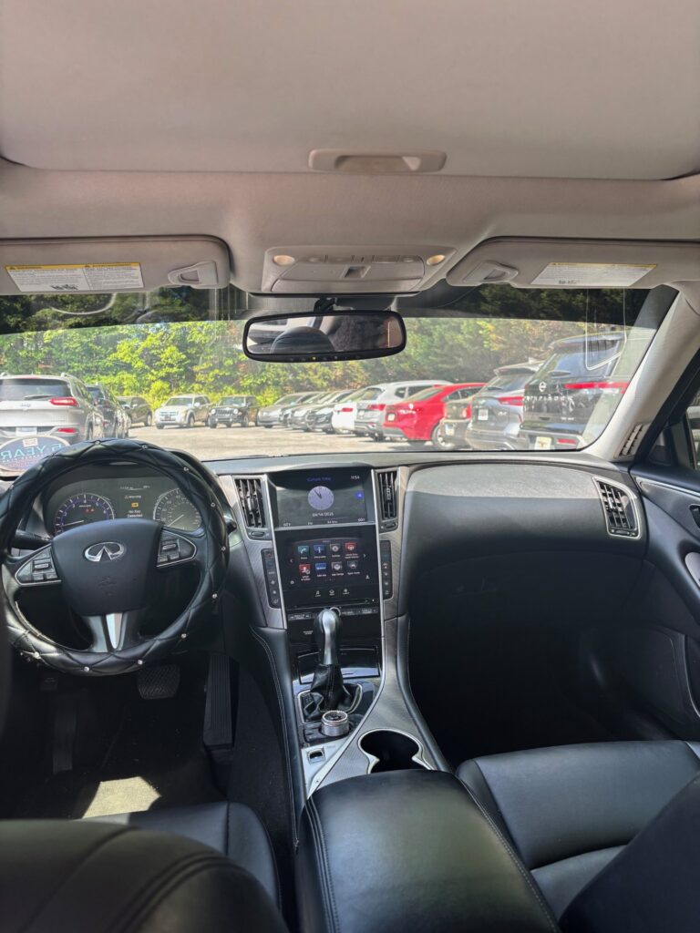 Inside view of a luxury car cabin with a black leather steering wheel, center touchscreen, gear shifter, and cupholders in the front console.