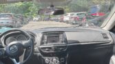 Interior of a car seen from the back seat: steering wheel, center console, gear shift, and dashboard with parked cars outside through the windshield