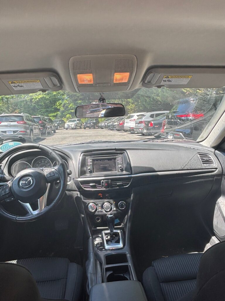 Interior of a car seen from the back seat: steering wheel, center console, gear shift, and dashboard with parked cars outside through the windshield