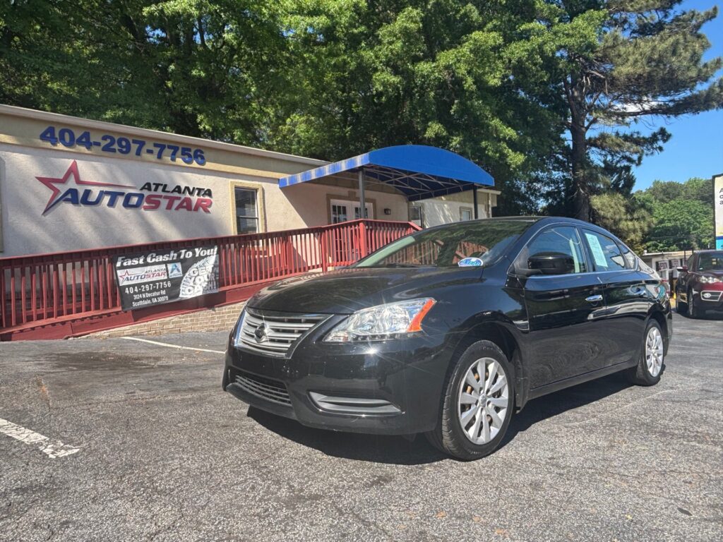 Black sedan parked in front of Atlanta AutoStar dealership with a blue awning and banner reading Fast Cash To You in the lot behind a red railing.