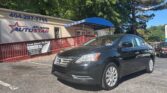 Black sedan parked in front of Atlanta AutoStar dealership with a blue awning and banner reading Fast Cash To You in the lot behind a red railing.