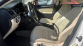 Beige interior of a sedan: driver and front passenger seats, steering wheel, and dashboard visible from the open driver’s door in daylight.