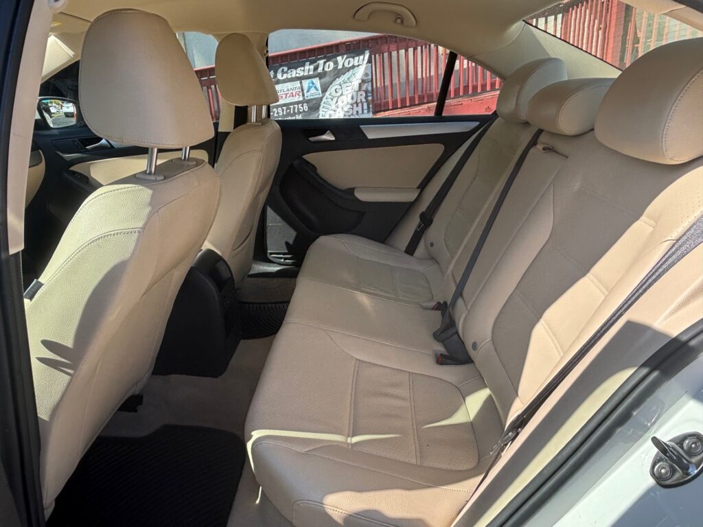 Beige leather backseat of a car with three headrests and seat belts visible in daylight outside window.