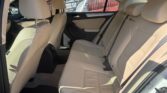 Beige leather backseat of a car with three headrests and seat belts visible in daylight outside window.