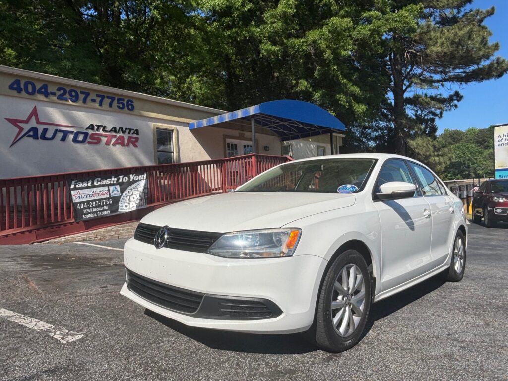 White Volkswagen sedan parked in front of Atlanta AutoStar dealership with a blue awning and red railing.