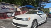 White Volkswagen sedan parked in front of Atlanta AutoStar dealership with a blue awning and red railing.