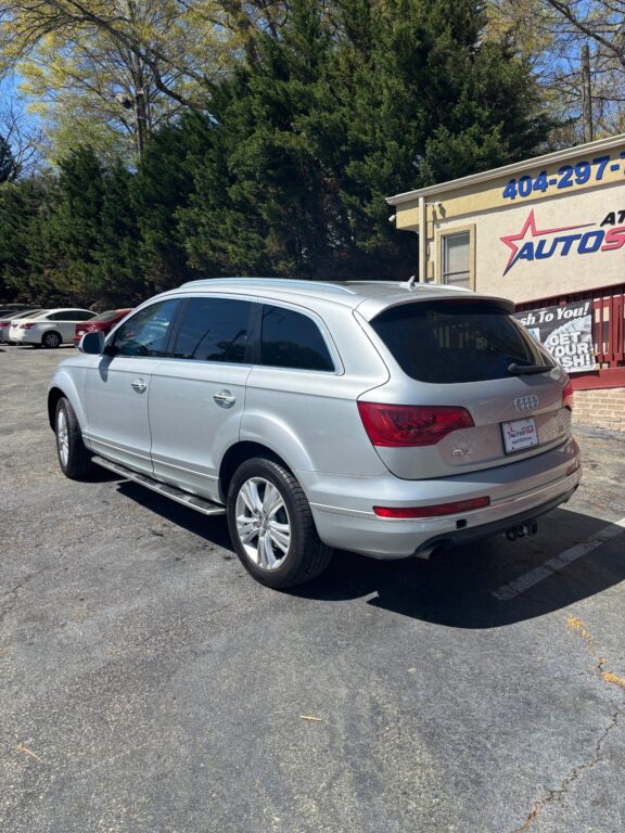 Rear three-quarter view of a silver Audi SUV parked in a car dealership lot, with a beige building and sign in the background.