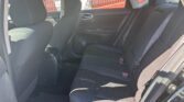 Interior of a dark fabric-sedan back seat area with a three-seat bench and visible seat belts, front seat in view, Sunlit window on the right.