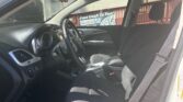 Interior view from the driver’s side showing steering wheel, dashboard, center console, and front seats inside a car. Outside are a red fence and a sign visible through the windows.