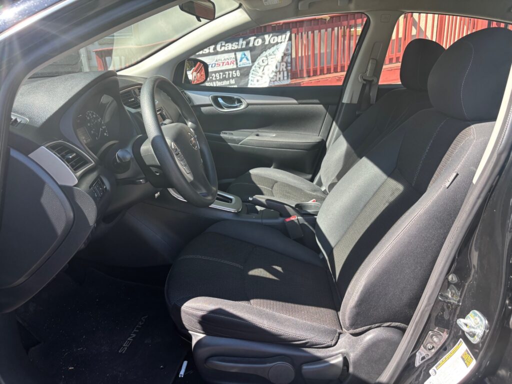 Front interior of a black sedan from the driver’s side showing the steering wheel, dashboard, center console, and black cloth seats.