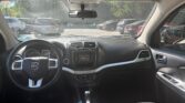 Driver's-seat view of a Dodge interior: steering wheel, center console, and dashboard with radio and climate controls; parking lot seen through windshield