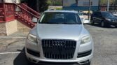 Front view of a silver Audi SUV parked in a lot beside a brick building with a blue canopy and red railing; large billboard in the background.