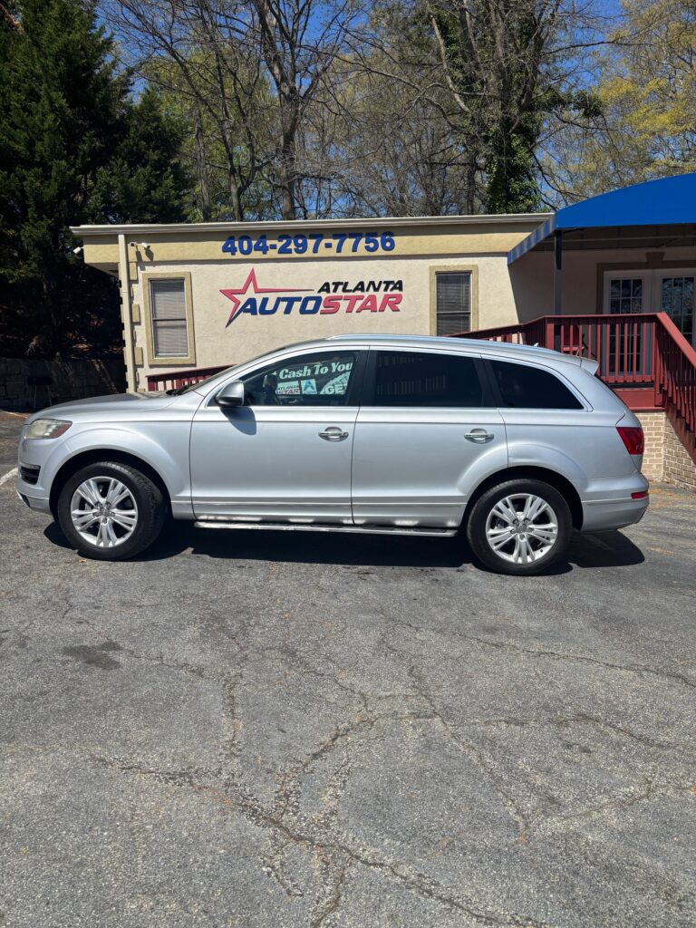 Silver SUV parked in front of a beige Atlanta Auto Star dealership building with a large blue phone number on the wall.
