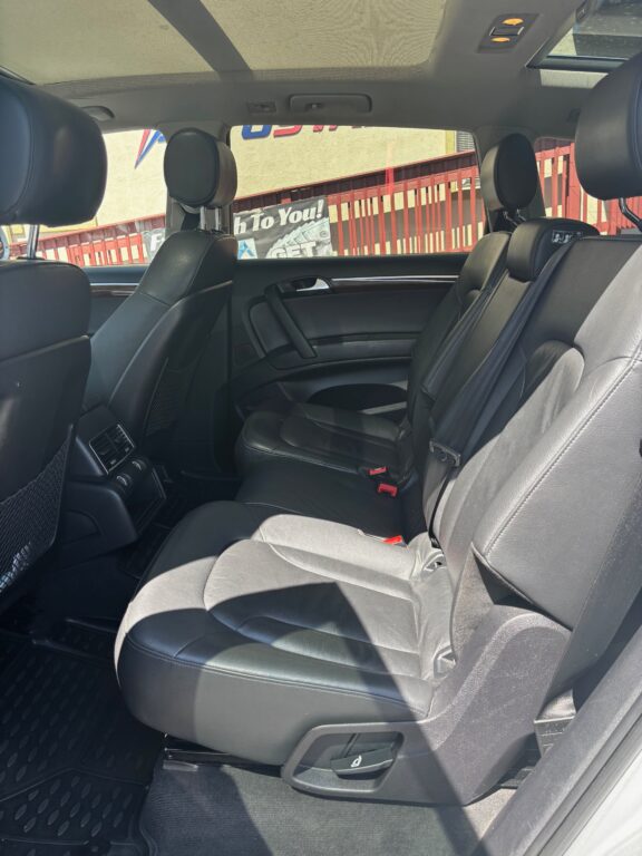 Rear interior of a black leather SUV, three-seat row with headrests and red seatbelt buckles.