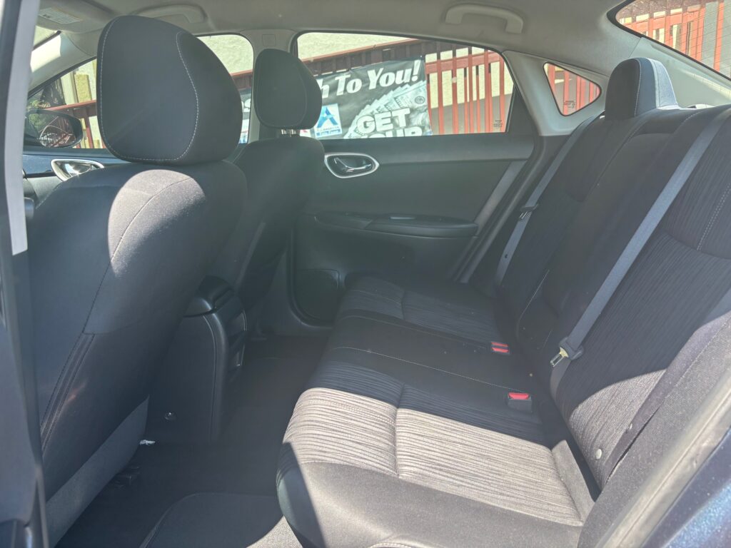 Back seat of a dark cloth interior car with three seats, headrests, and visible seat belts.