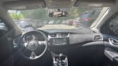 Interior of a car viewed from the back seat, showing the steering wheel, center console, and dashboard with a parking lot of cars outside through the windshield.