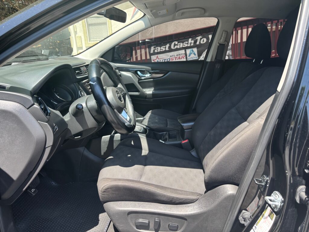 Interior of a black car showing the driver’s seat, front passenger seat, steering wheel, and center console seen from the open driver’s door.