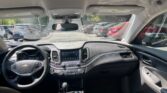 Interior view of a Chevrolet SUV: left-hand steering wheel, central touchscreen, climate controls, gear shifter, and cupholders with black upholstery; parked cars visible through the windows.