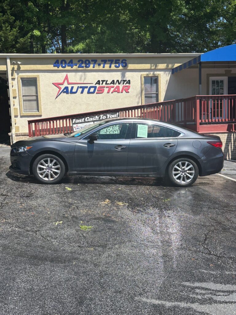 Gray four-door sedan parked in front of a beige building labeled Atlanta AutoStar, with a blue phone number sign above the entrance and a red railing in the background.