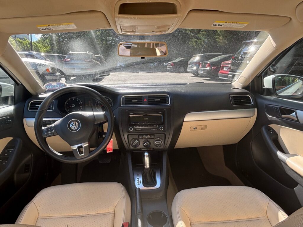 Interior of a car cockpit with beige seats, black dashboard, and steering wheel viewed from the front passenger seat.