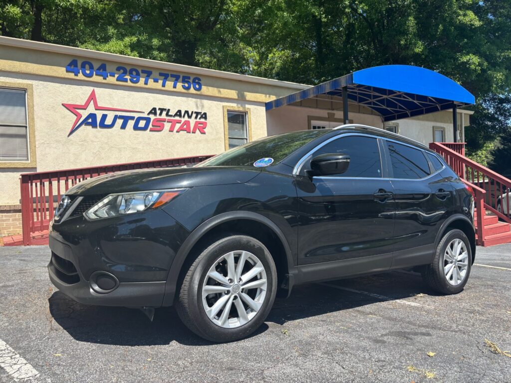 Black SUV parked outside a beige Atlanta AutoStar dealership with blue signboard and a red railing staircase behind it.