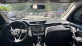 Interior view from the driver’s seat: steering wheel, center console with radio, and gear shifter, parking lot seen through the windshield with multiple cars