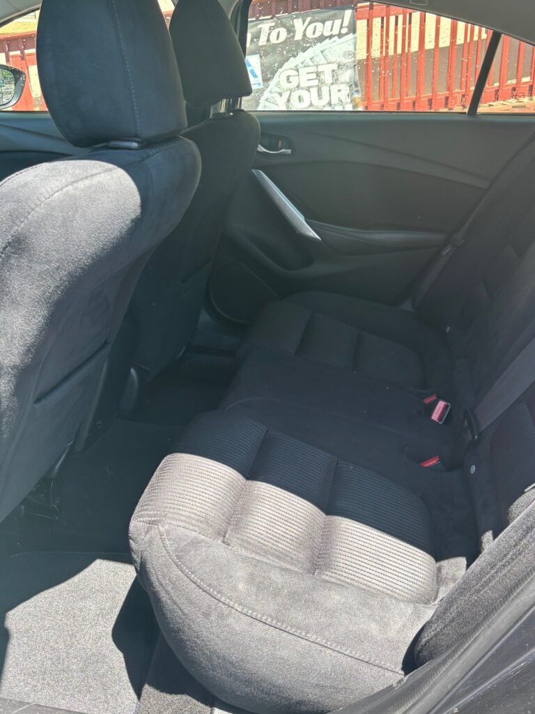 Back seat area of a dark cloth sedan, rear doors, and seat belts visible in daylight outside the window.