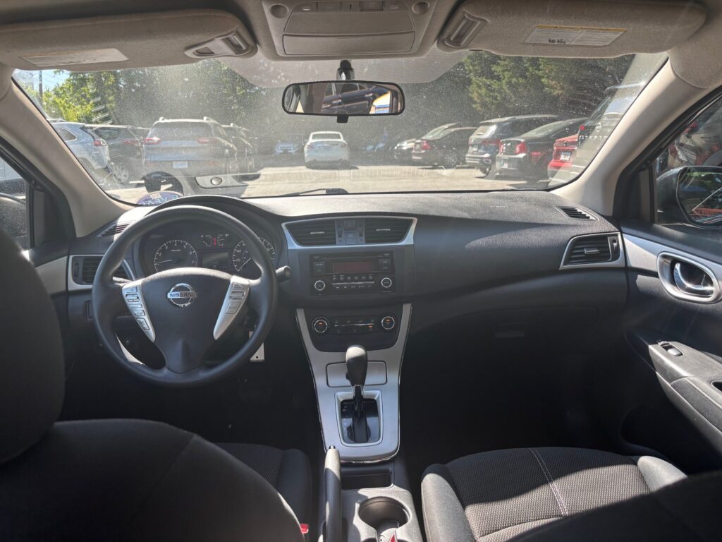 Interior view of a Nissan sedan cockpit: steering wheel, center console, and front seats seen from the back seat
