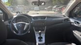 Interior view of a Nissan sedan cockpit: steering wheel, center console, and front seats seen from the back seat