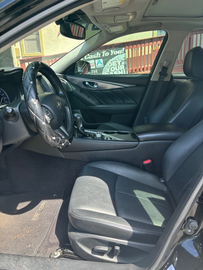 Front interior of a black car with a quilted steering wheel cover, leather seats, and a center console visible.
