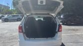 White SUV with its tailgate open, showing the dark cargo area in a sunny parking lot. Gobetween vehicles and trees in the background.