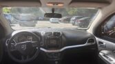 View from the front seat of a car: steering wheel, center console, and dashboard visible; parking lot with many cars through the windshield