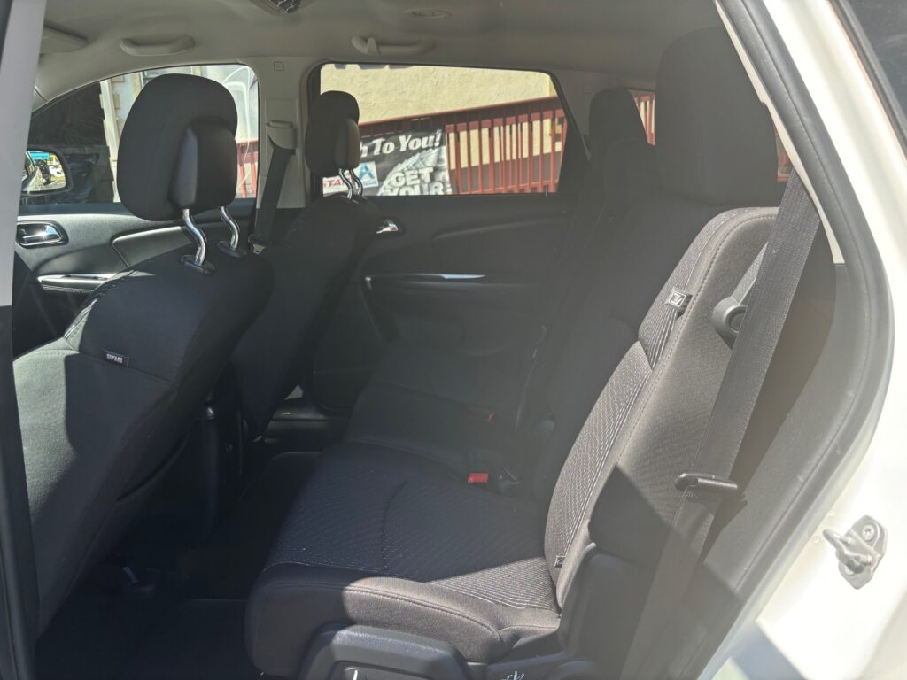 Rear passenger area of a black fabric SUV with two front seats, headrests, and visible seat belts in daylight outside the window