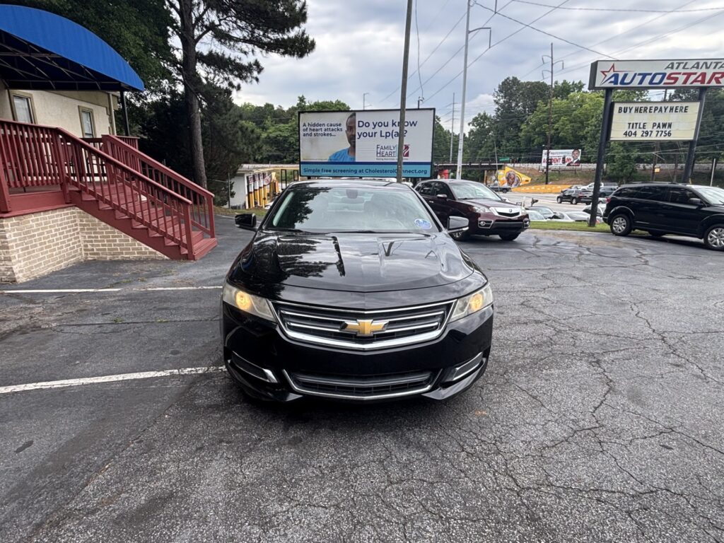 Black Chevrolet driving up in a parking lot with a blue awning building on the left and a billboard in the background.