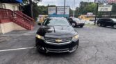 Black Chevrolet driving up in a parking lot with a blue awning building on the left and a billboard in the background.