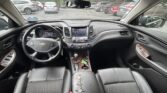 Front car cabin with steering wheel, dashboard touchscreen, and center console; black leather seats with a torn armrest cover in the foreground.
