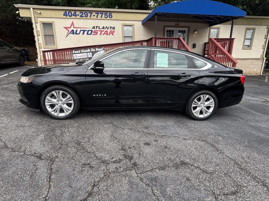 Black Chevrolet Impala sedan parked in a lot in front of an Atlanta AutoStar dealership with a blue canopy above the entrance.