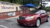 Red sedan parked in front of the Atlanta AutoStar dealership, blue awning overhead, with the phone number 404-297-7756 on the building sign.
