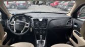 View from the back seat of a beige-car interior showing steering wheel, center console, and gear shifter facing a parking lot through the windshield.