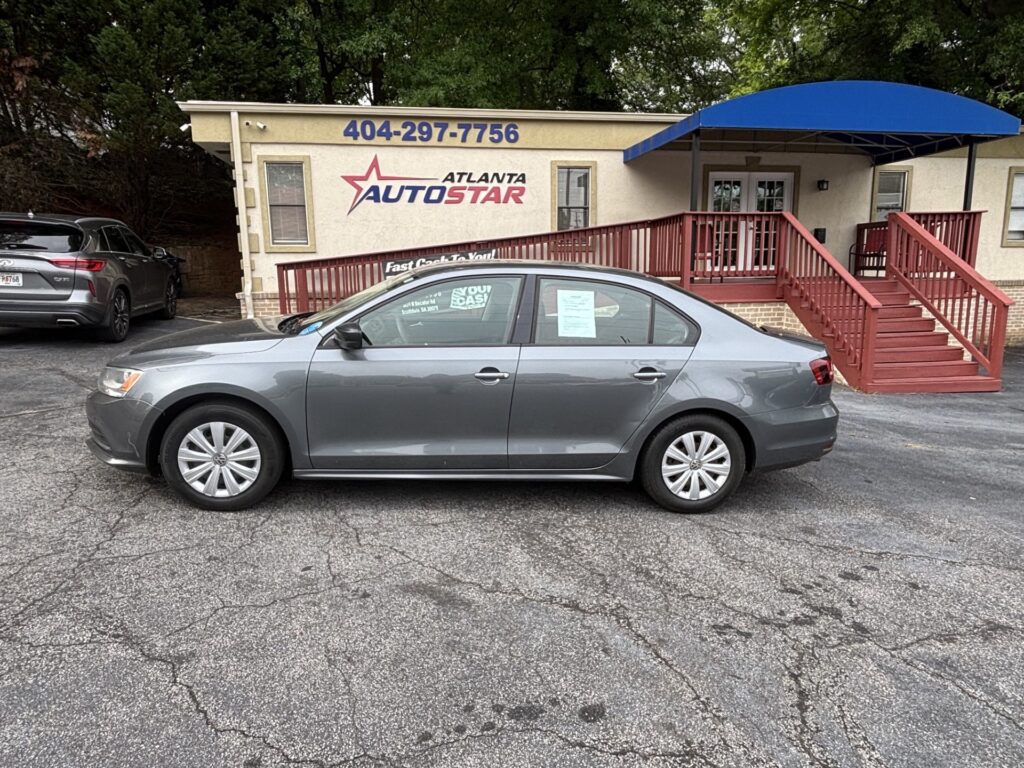 Gray sedan parked in front of a beige building with a blue awning and red stairs; dealership sign reads 'Atlanta AutoStar' and phone number 404-297-7756