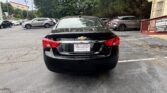 Rear view of a black Chevrolet sedan in a car dealership lot, with other cars and a building in the background (Atlanta Auto Star plate).
