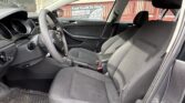 Interior of a compact car showing the driver's seat, steering wheel, and front passenger seat with dark upholstery and floor mats. The view is from the open passenger side door.