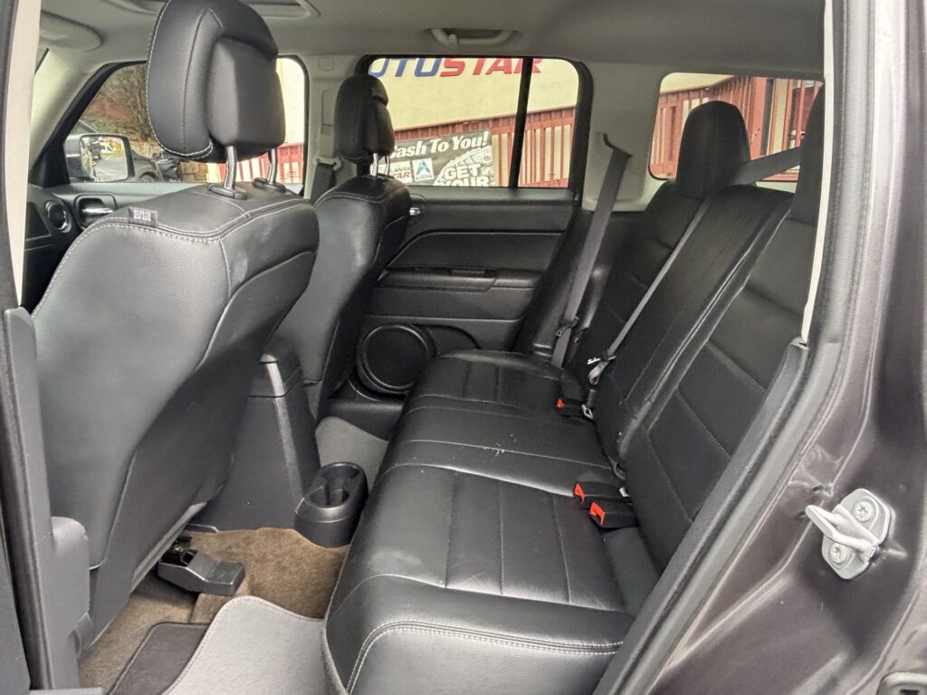 Dark leather back seat area of an SUV, showing two headrests, seat belts, and a center cup holder/console.