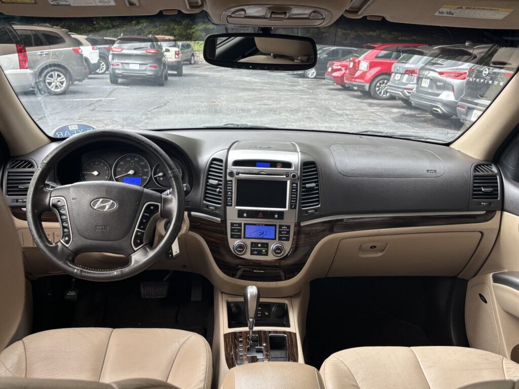 View from the driver’s seat inside a beige SUV, showing steering wheel, dashboard, and center console with gear shifter.