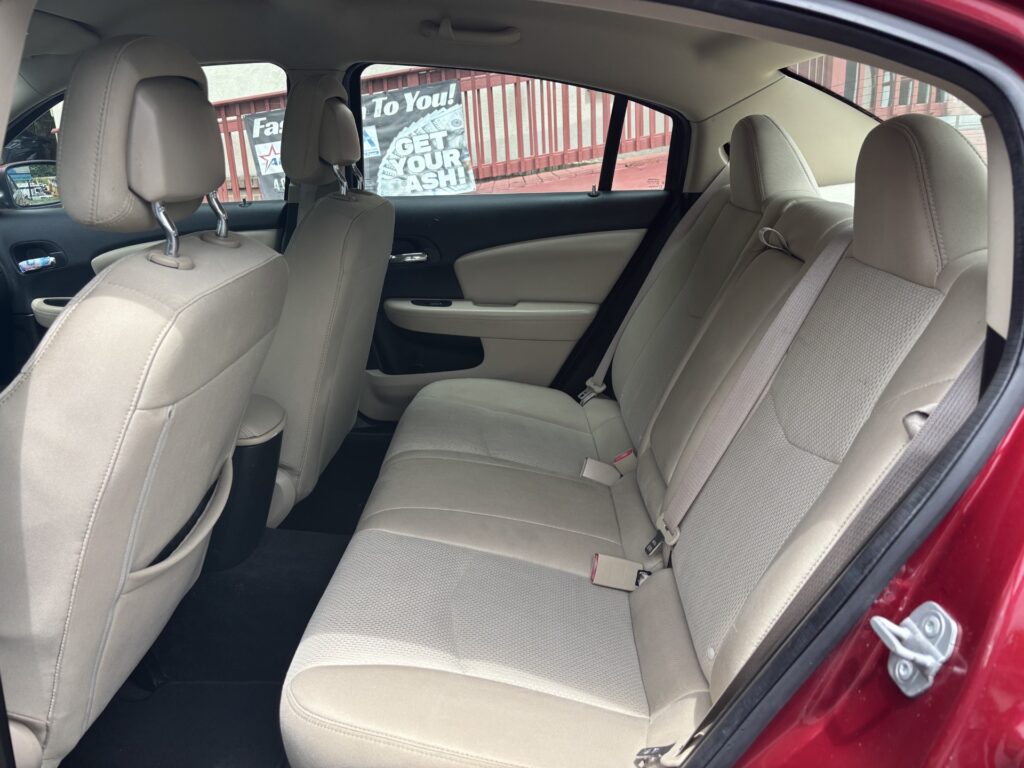 Rear passenger area of a beige fabric sedan showing three-seat bench, headrests, and seat belts