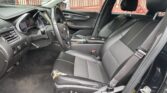 Front passenger and driver seats of a black leather car interior; visible wear on the driver seat with torn upholstery and exposed foam. Steering wheel, dashboard, and center console in view.