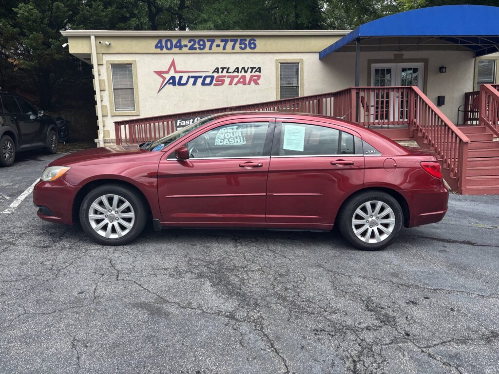 Maroon four-door sedan parked in front of a beige building with an Atlanta Auto Star sign and a blue awning.