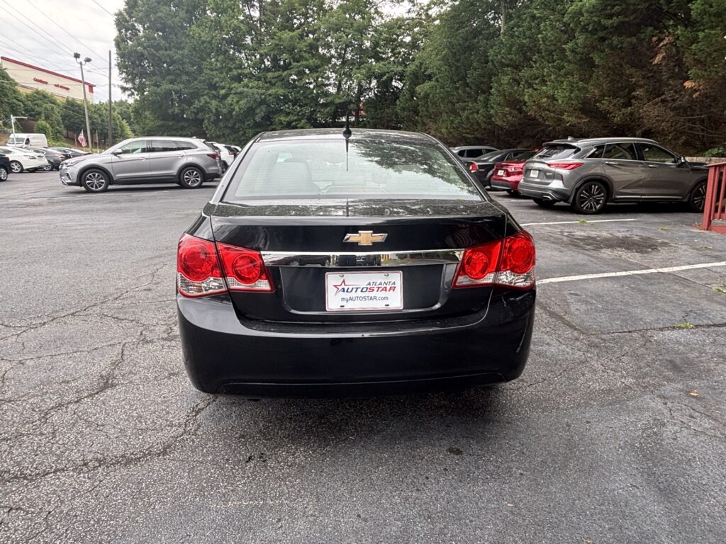 Rear view of a black Chevrolet sedan in a car dealership lot, with other vehicles and trees in the background; dealership plate reads 'Atlanta Autostar'.
