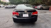 Rear view of a black Chevrolet sedan in a car dealership lot, with other vehicles and trees in the background; dealership plate reads 'Atlanta Autostar'.