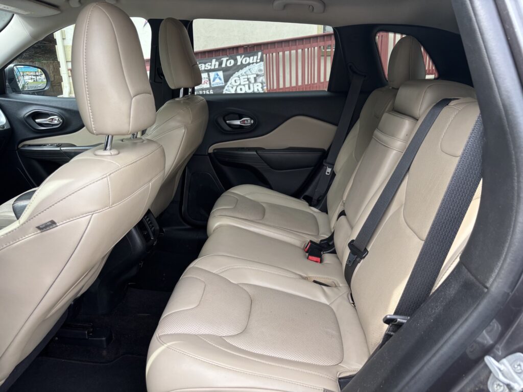 Beige leather SUV rear seating with three seats, headrests, and visible seat belts.